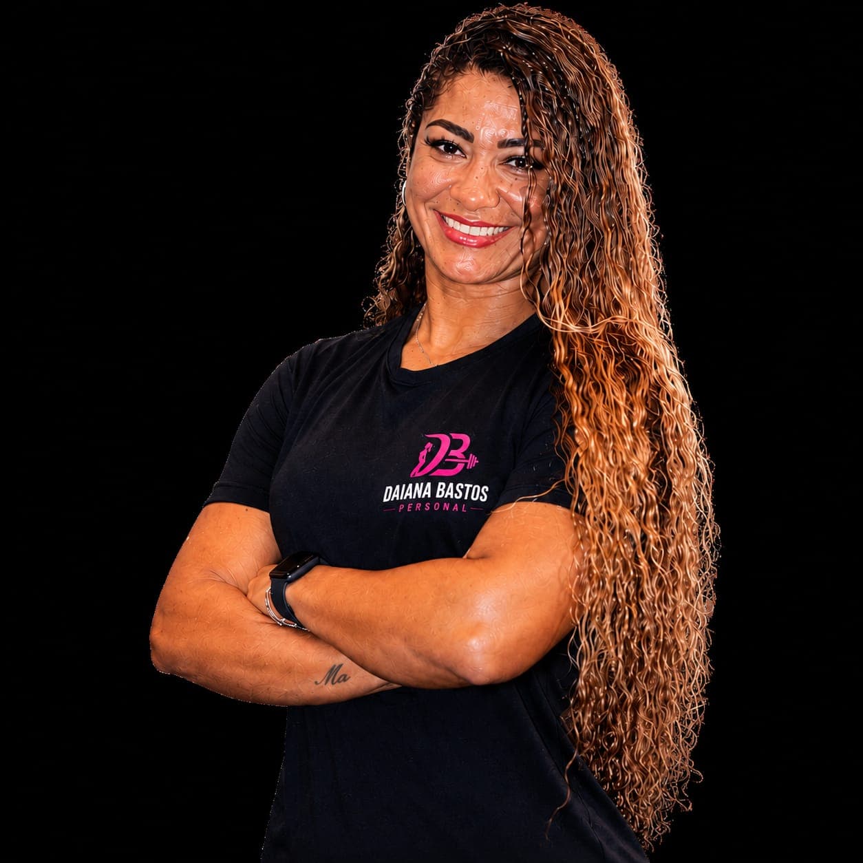 Daiana Bastos, personal trainer, sorrindo de braços cruzados com a camiseta da marca